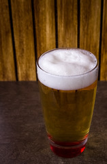 Glass full of beer on flat base and wooden background 