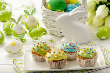 Easter decoration - colored eggs, muffins and bunny on wooden background.