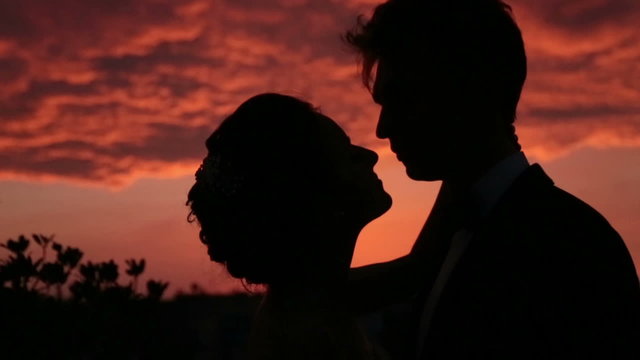 Silhouettes of romantic wedding couple lissing on the red sunset background close up