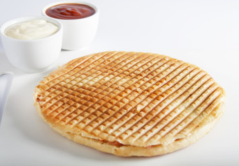 Toast with cheese and cured meat products placed on the white plastic cutting board besides ketchup and mayonnaise in white bowls.