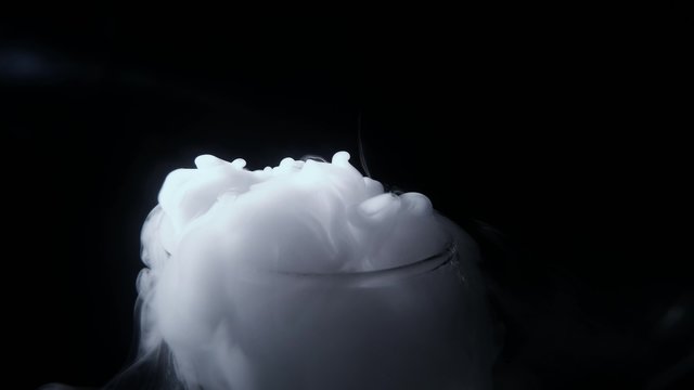 White Smoke Curls at the Outlet of Glass Vessel on a Background of Total Darkness Close up
