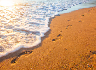beach, wave and footprints at sunset time
