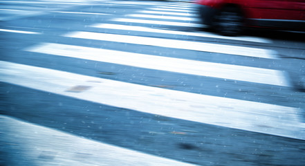 Motion blurred high speed red vehicle runs across the pedestrian crossing in the rainy city....