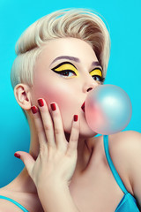 Fashionable girl with a stylish haircut inflates a chewing gum. The girl in the studio on a blue...