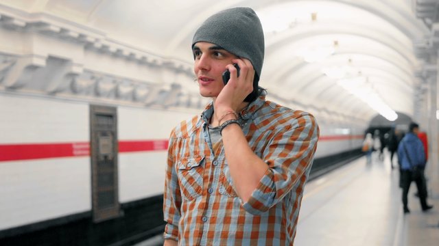 Young caucasian man talking on cellphone on subway platform