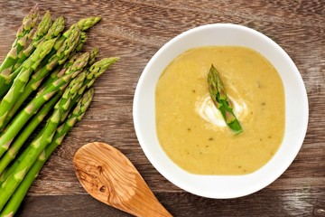 Creamy asparagus soup in a white bowl, overhead scene against a rustic wood background