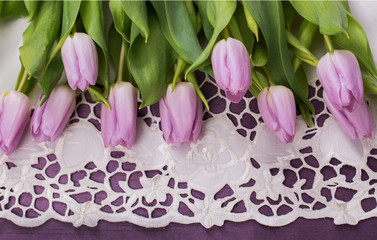 Wiosenny pastelowy bukiet liliowych tulipanów na fioletowym tle na białym obrusie z haftem richelieu