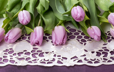 Wiosenny pastelowy bukiet liliowych tulipanów na fioletowym tle na białym obrusie z haftem...