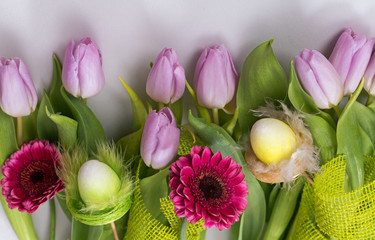 Wiosenny pastelowy bukiet z liliowych tulipanów i różowych gerber na białym tle z jutową jasnozieloną taśmą ozdobną i ozdobami wielkanocnymi - obrazy, fototapety, plakaty