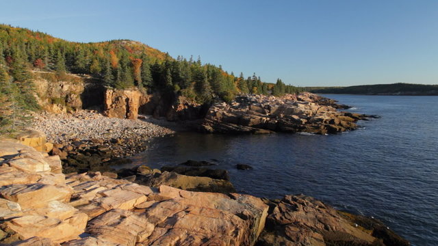 The rocky beach of Monument Cove, with Autumn foliage on Gorham Mountain in the background, in Acadia National Park in early morning light.