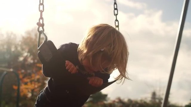 A little girl laying down on a swing and smiling, and then yelling, with lens flare, slow motion