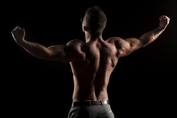 Fototapeta premium back view of naked muscular man in pants on black