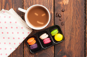 Mini macaron cookies and cup of coffee on wooden table backgroun