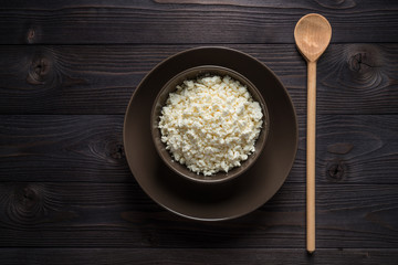 cottage cheese in a brown bowl on a dark wooden background