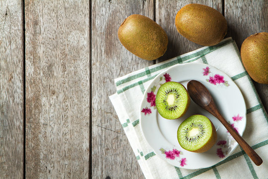 KIwi fruit on dish and spoon on wooden background.