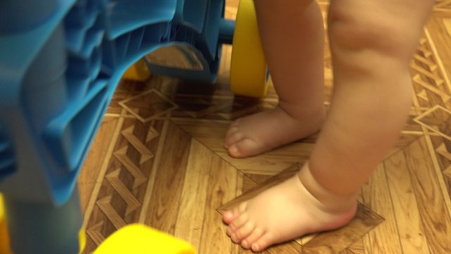 Newborn Baby Feet Next to Plastic Bicycle. Closeup. 4K UltraHD video.