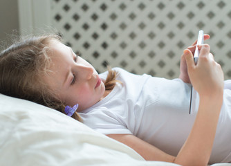 Little girl lying with tablet pc in bed.