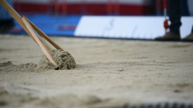 Men raking the sand after a long jump in the sandpit