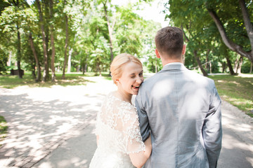 Bride and groom walking away in summer park outdoors