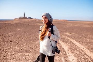Young female photographer in sweater and hat walking with camera, backpack and tripod on the...