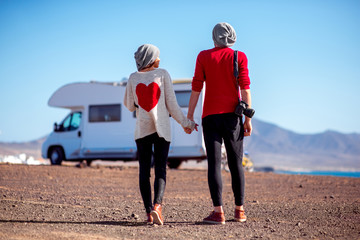 Young stylish couple in sweaters with heart shape standing on the deserted seaside with mountains...