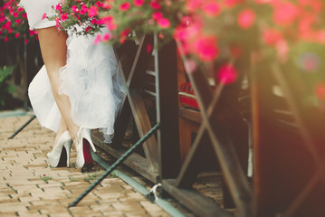 Beautiful legs of a bride standing near a fence with flowers.