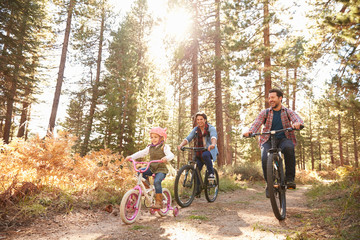 Happy family riding bicycle on dirt track in forest