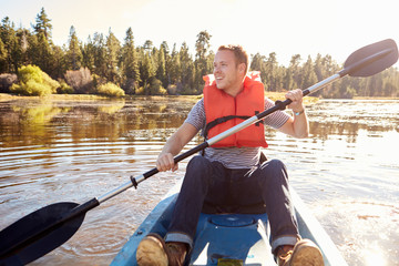 Man Wearing Life Preserver Rowing Kayak On Lake