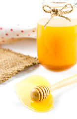 Glass can full of honey and wooden stick on a white background.