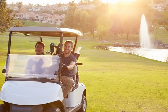 Male Golfers Driving Buggy Along Fairway Of Golf Course