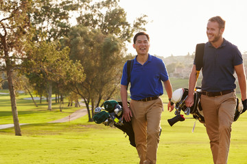 Two Male Golfers Walking Along Fairway Carrying Bags