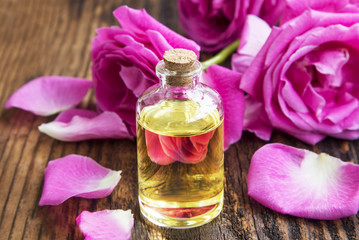 Rose essential oil with pink roses and petals on wooden board