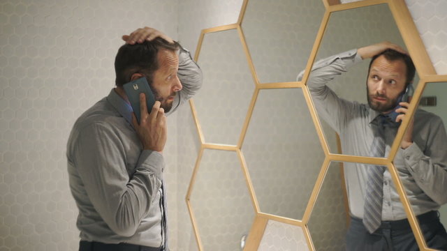 Young businessman talking on cellphone and checking look in mirror
