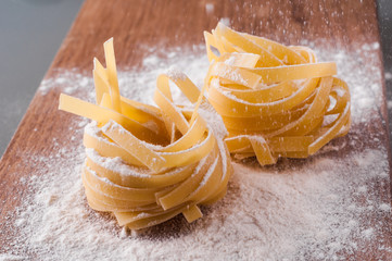 raw tagliatelle with flour on brown wooden table