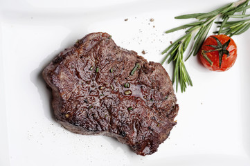 On a white plate delicious piece of tender steak, meat, served with cranberry sauce and spiced with rosemary, cherry tomato.