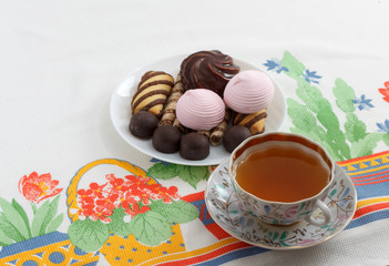 Traditional breakfast concept with colorful cup of tea, sweets and biscuits on white tablecloth with colorful print