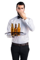 Waiter with beer bottles on the tray covering his mouth