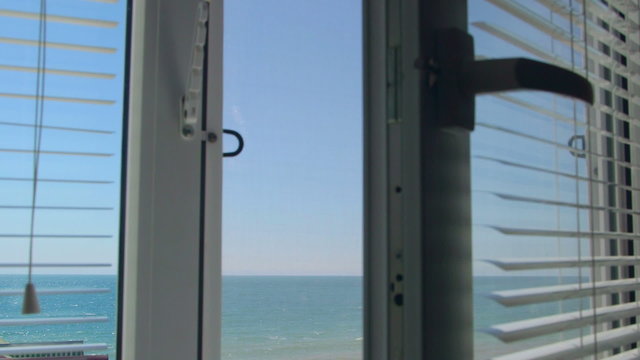 View from the open window with blinds on the sea in summer