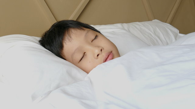 Young asian boy sleeping on bed and smiles after wake up 