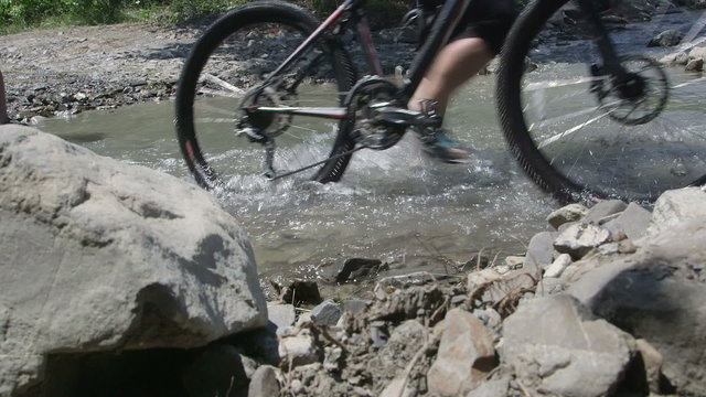 Cyclists crossing water stream pushing mountain bikes during cross country cycling in summer