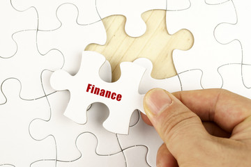 Finance concept. Hand holding piece of jigsaw puzzle showing FINANCE word.