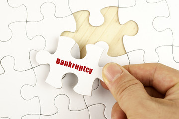 Finance concept. Hand holding piece of jigsaw puzzle showing BANKRUPTCY word.