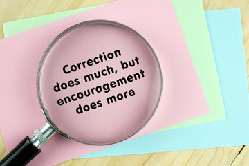 Magnifying glass on papers with word quote of "Correction does much,but encouragement does more" written on it.