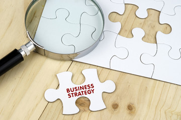 Business concept.Magnifying glass on jigsaw puzzle and a puzzle piece written with BUSINESS...