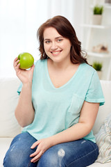 happy plus size woman eating green apple at home