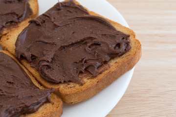 Chocolate peanut butter on hard toast on a white plate and a wood table top close view.