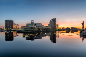 Orange sunrise at Salford Quays with blue sky and clear reflections in canal. - 104839626