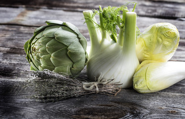 vegetable still life - fresh artichoke, fennel, endives and thyme on genuine wood background for home-made vegetarian cooking, studio shot