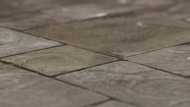 Rain drops rippling in a puddle on wet patio garden driveway natural stone paving slab 