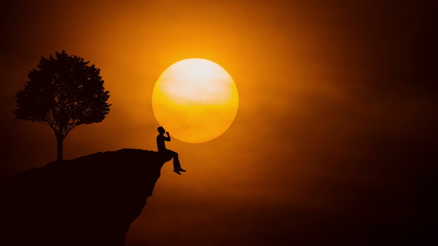 The man sit on the edge of a cliff on the background of sunset. Real time capture